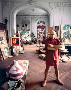 an older man standing in a room with many paintings on the walls and flooring