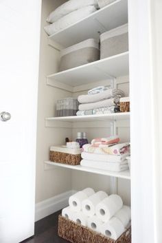 an organized closet with white linens and baskets on the shelves, including toilet paper