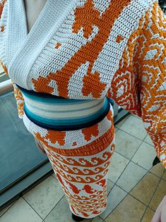 an orange and white crocheted sweater is hanging on a mannequin