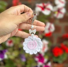 a hand holding a crocheted key chain with a pink and white flower on it