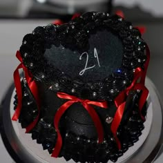 a cake decorated with black and red ribbon on top of a silver plate topped with a heart