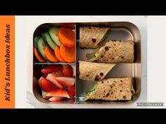 a metal container filled with fruit and veggies next to a sandwich cut in half