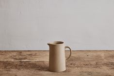 a brown jug sitting on top of a wooden table next to a white painted wall