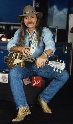 a man sitting on top of a chair with a guitar in his lap and wearing a cowboy hat