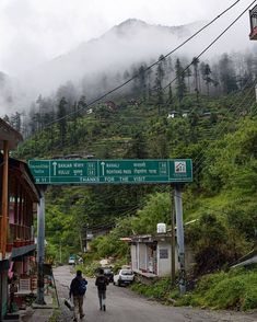 two people are walking down the street in front of some houses and mountains with clouds