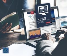 two people sitting at a table with laptops and books on their laps, reading news