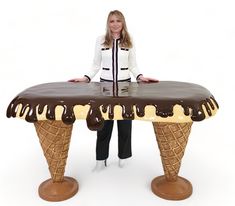 a woman standing next to an ice cream cone shaped table with chocolate sauce on top