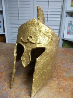 a helmet made out of gold foil sitting on top of a table next to a wall