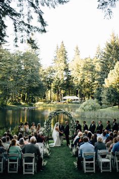 a wedding ceremony in front of a lake with people sitting at the alter and looking on