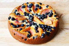 a cake with blueberries and peaches on it sitting on a wooden table top