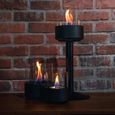 three lit candles sitting on top of a wooden table in front of a brick wall