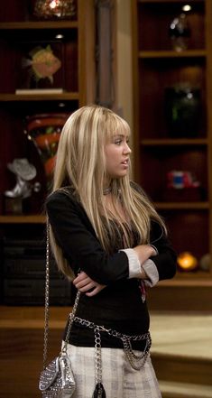 the young blonde woman is standing in front of a book shelf with her arms crossed