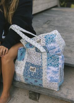 a woman sitting on the steps holding a blue and white quilted bag with her legs crossed