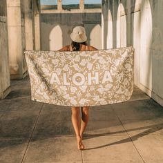 a woman is walking down the sidewalk holding a towel that says aloha on it