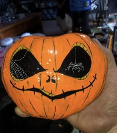 a hand holding a pumpkin with eyes painted on it