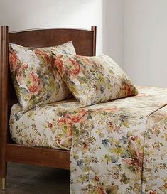 a bed with floral sheets and pillows on top of it next to a wooden headboard