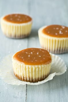 three cupcakes with caramel sauce on top are sitting on paper wrappers