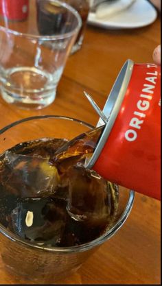 a person pouring ice into a glass on top of a wooden table