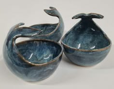 two blue bowls sitting next to each other on a white tableclothed surface, with one bowl shaped like a bird and the other is shaped like an upside down