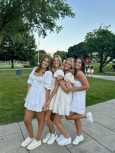 three girls in white dresses posing for the camera with their arms around each other and smiling