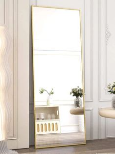 a large mirror sitting on top of a wooden floor next to a vase filled with flowers