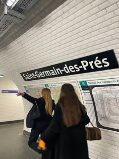 two women are standing in front of a subway sign and pointing at the map on the wall