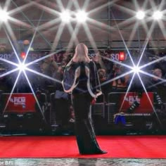 a woman standing on top of a red carpet in front of some bright spotlights