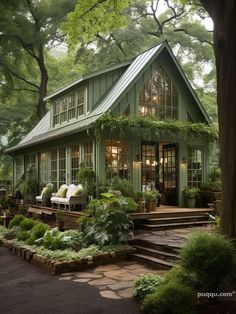 a small green house surrounded by greenery and lots of trees in the background with stairs leading up to it