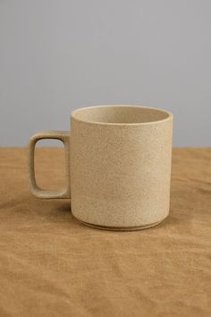 a white cup sitting on top of a wooden table next to a brown cloth covered surface