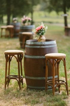 two stools are next to a barrel with flowers on it and another stool is in the grass