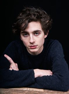 a young man sitting at a table with his arms crossed and looking to the side