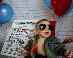 a young boy wearing sunglasses sitting in front of some balloons and signs with words on them