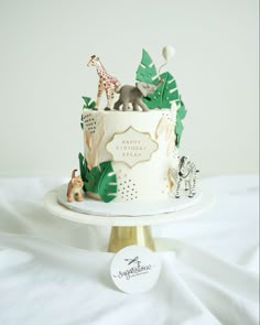 a birthday cake decorated with jungle animals and palm leaves on a white tablecloth background