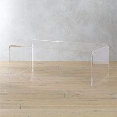 a clear acrylic table sitting on top of a hard wood floor next to a white wall