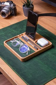 a cell phone and some glasses are on a table next to a camera, with a plant in the background