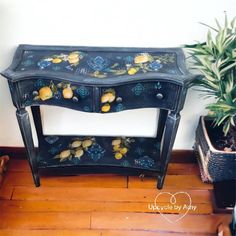 an ornate black painted console table with fruit and flowers on the top, next to a potted plant