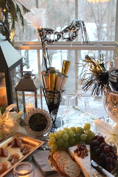 an assortment of cheeses, crackers and grapes on a table in front of a window