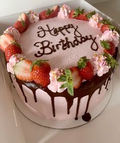 a birthday cake with strawberries and flowers on top is sitting in a white box