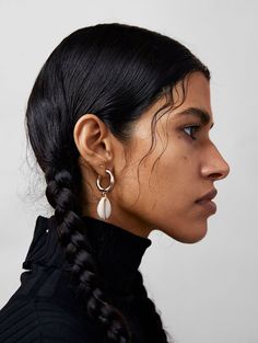 a woman with black hair wearing earrings and a black turtle - neck sweater is looking off to the side