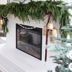 a fireplace decorated for christmas with evergreen garland and bells hanging from it's mantle