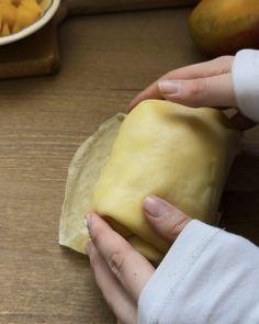 a person is holding a piece of cheese in their hand on a wooden table next to some fruit