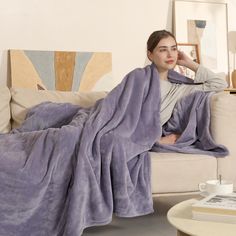 a woman sitting on a couch covered in a purple blanket with her hand under her chin