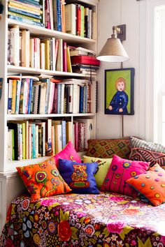 a living room filled with lots of colorful pillows and bookshelf full of books