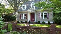 a gray house with red shutters on the front and side windows, surrounded by trees