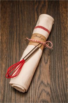 a napkin wrapped in twine with a red whisk on it sitting on top of a wooden table