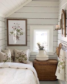 a white bed sitting under a window next to a basket filled with pillows and blankets