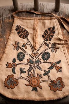 an old piece of cloth with flowers and leaves on it sitting on a wooden chair