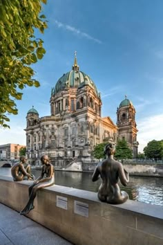 two statues sitting on the edge of a wall near water and buildings in the background