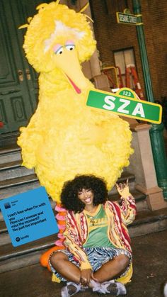 a woman sitting on the ground in front of a sesame street sign and chicken mascot