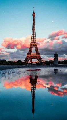 the eiffel tower is lit up at night with pink clouds in the background